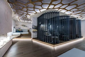 A modern interior with a geometric ceiling, a seating area with a sofa and chairs, and a wooden floor.