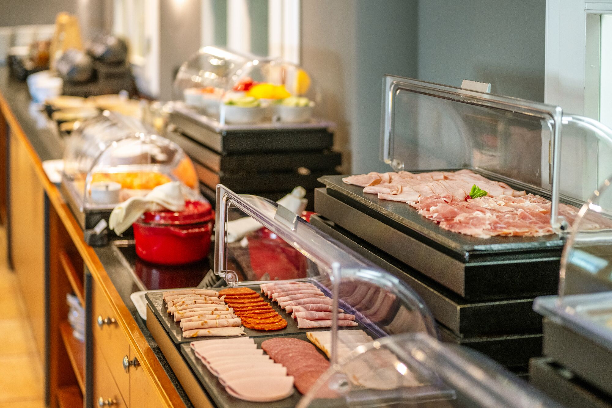 Un buffet proposant différentes sortes de viandes et un récipient rouge.
