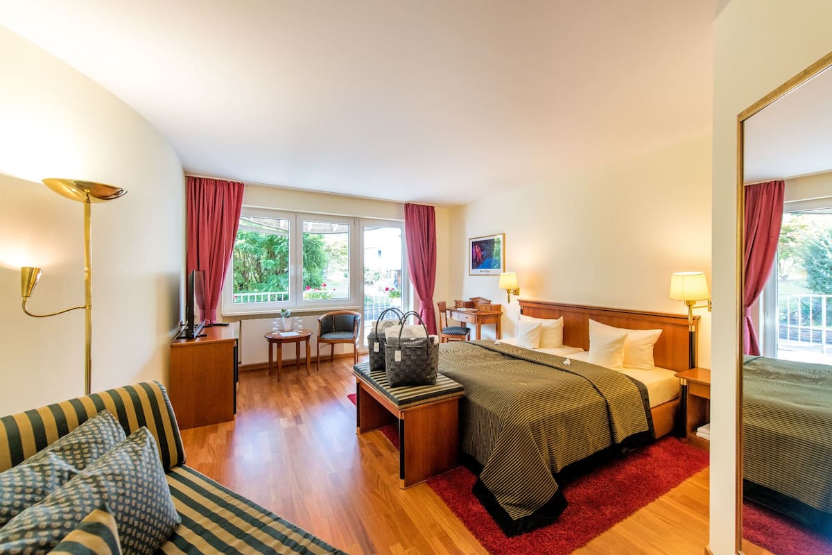 Ein Hotelzimmer mit Bett, Schreibtisch, Stuhl, Sofa, Lampe und einem fenster mit Vorhängen.