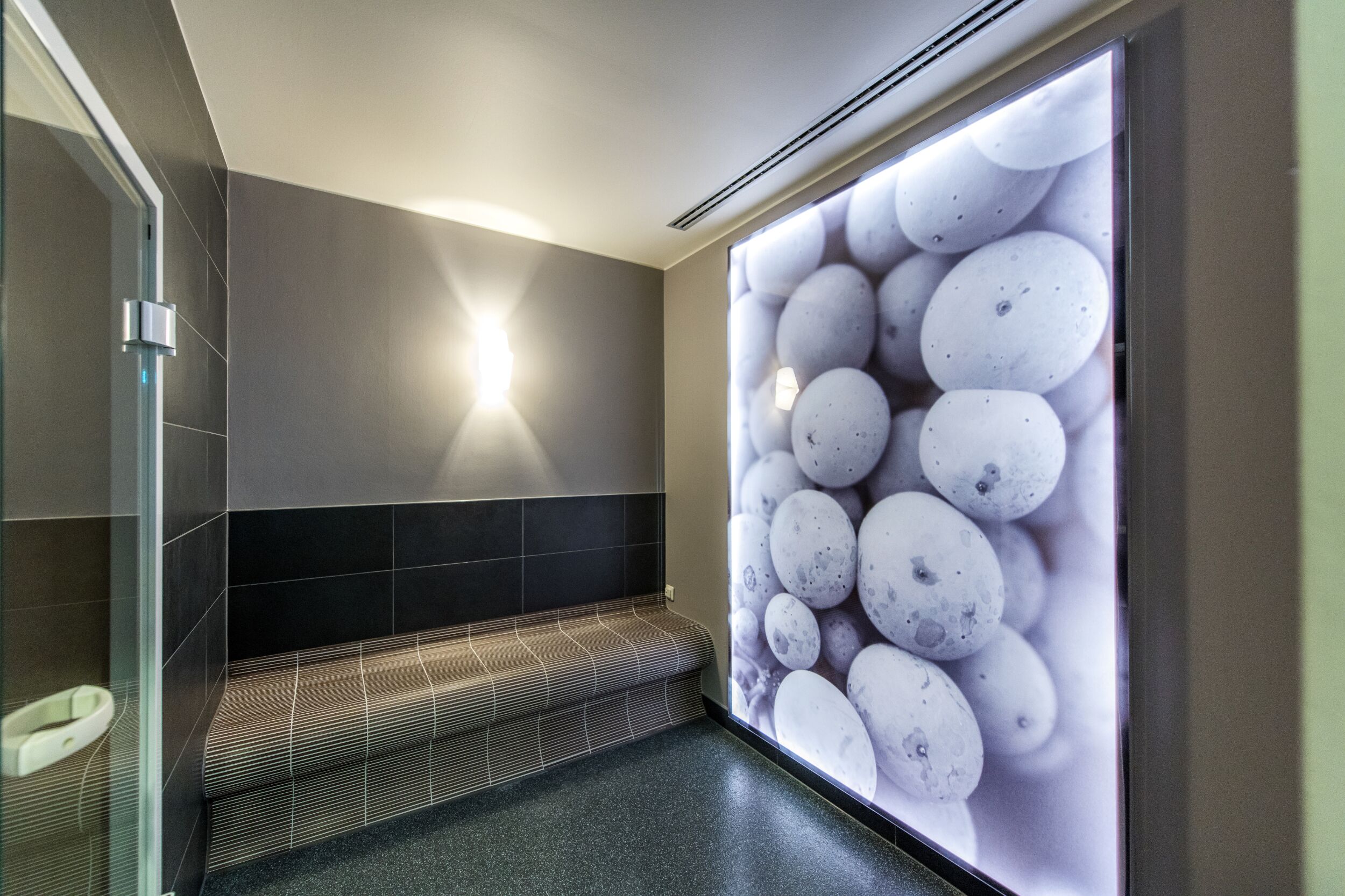 Un baño moderno con un banco, un panel de vidrio y una luz instalada en la pared.
