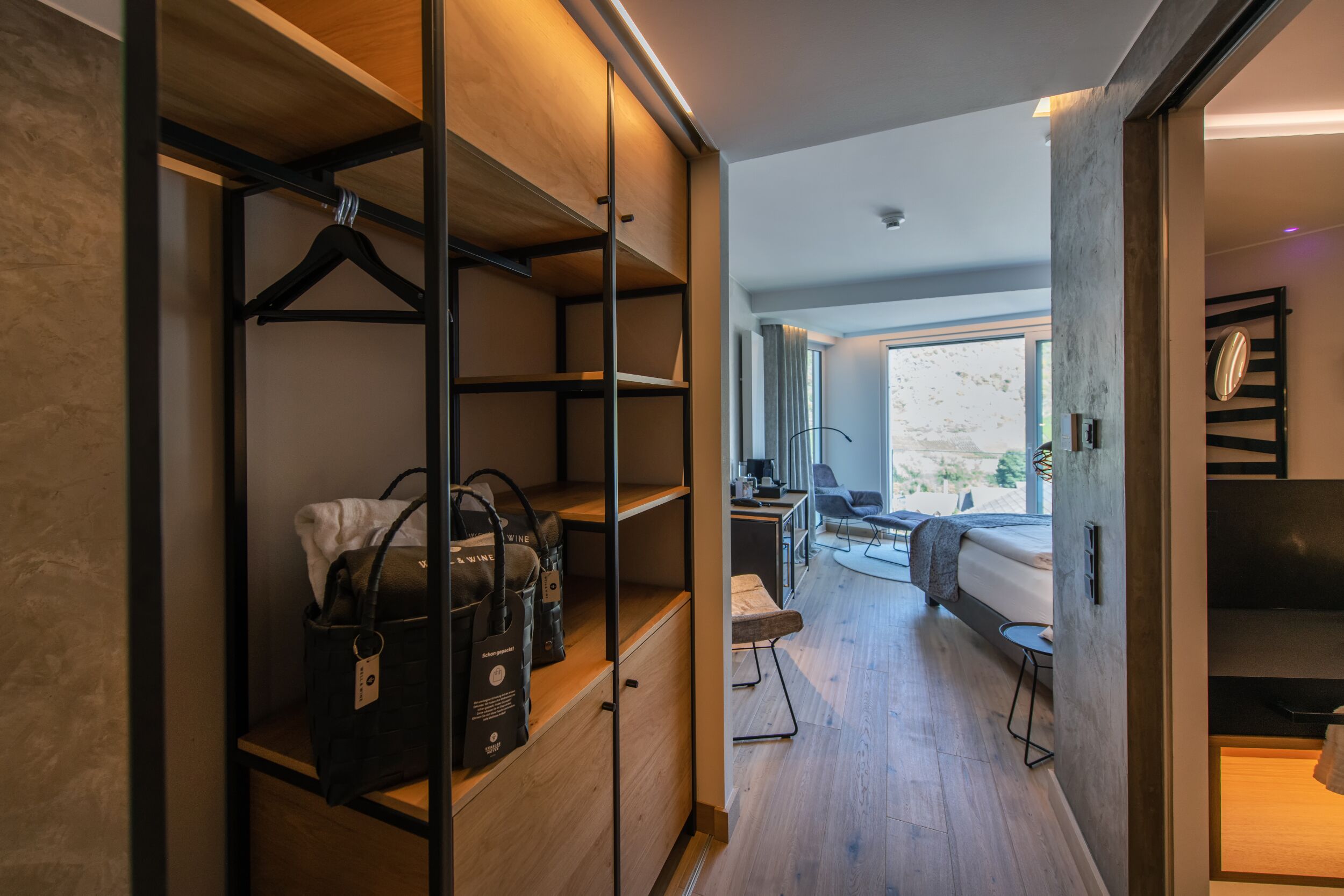 A modern hotel room with a walk-in closet, a bed, a desk, and a view of the outdoors.