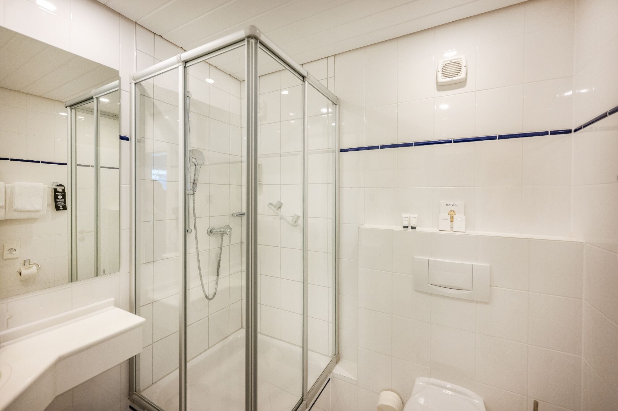 Un baño moderno con cabina de ducha de vidrio, un lavamanos blanco y un inodoro.