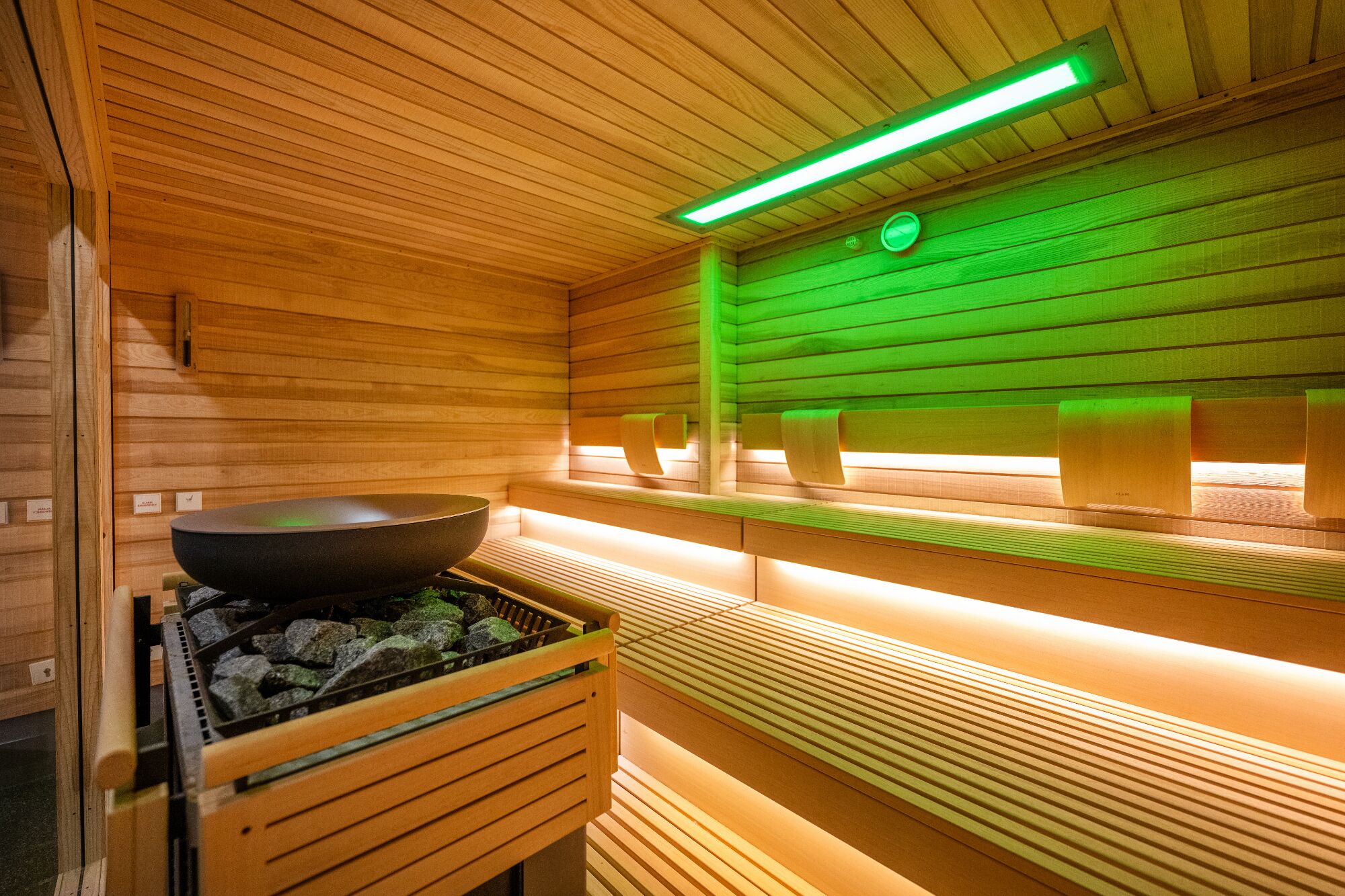 A sauna with wooden walls, benches, a large bowl, and green lighting.