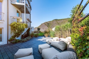 A patio with outdoor seating, a building with a balcony, and a hillside in the background. - Moselromantik Hotel Kessler Meyer (Cochem)