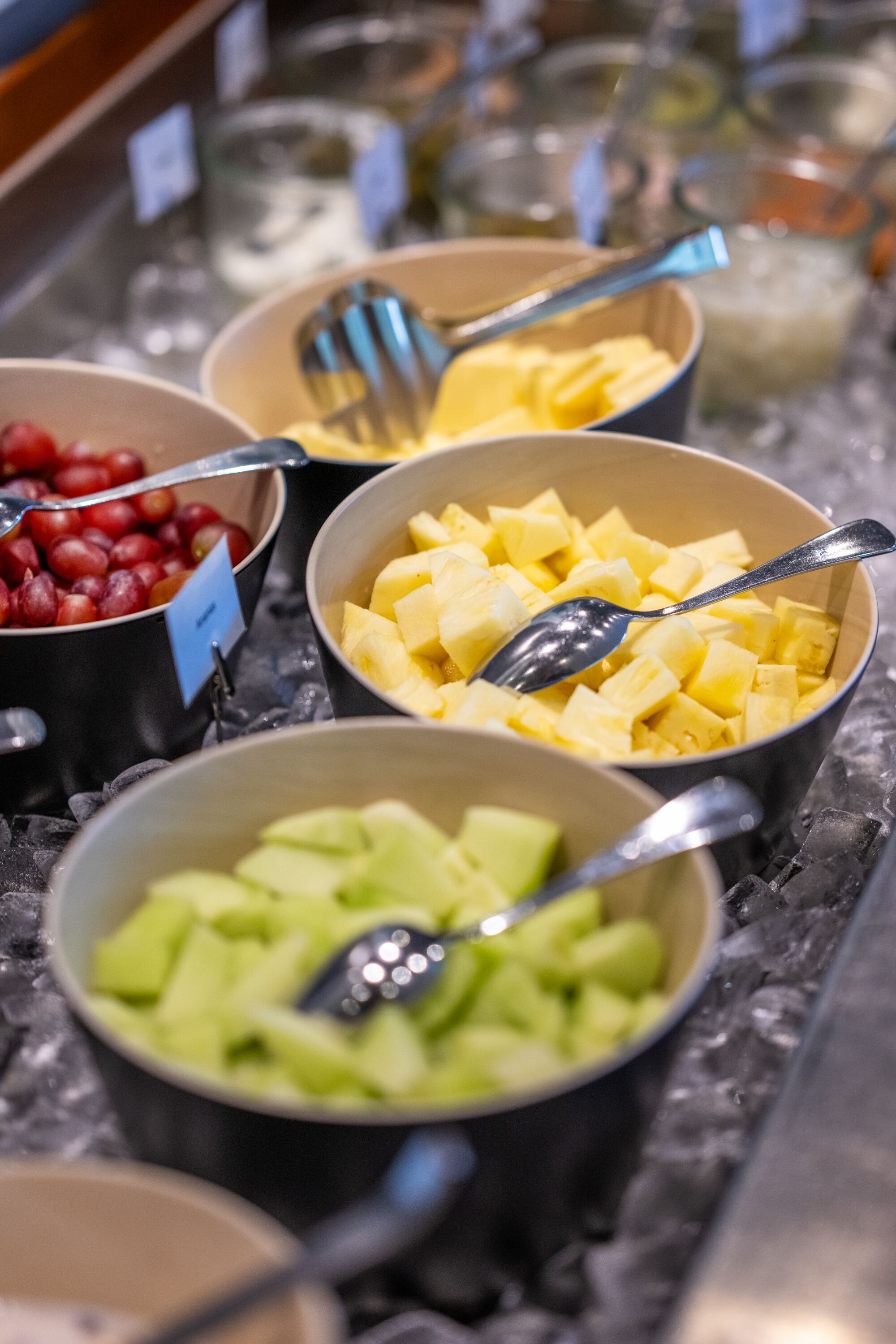 A buffet with various fruits and a spoon in each bowl.