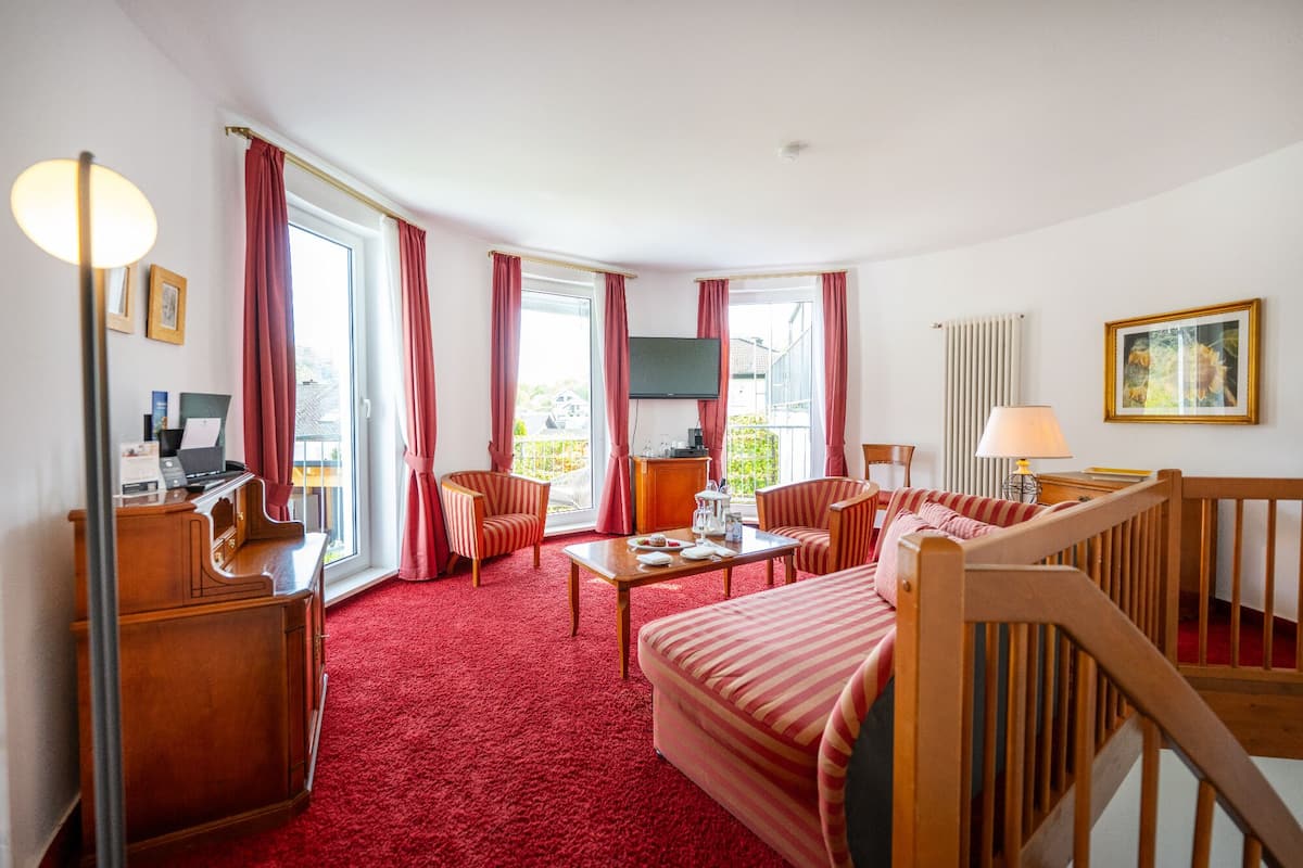 Ein Hotelzimmer mit rotem Teppich, einer Couch, einem Esstisch, einem Fernseher und einem Schreibtisch mit Computer.