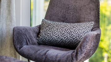 A modern armchair with a patterned cushion, positioned near a window with a view of greenery.