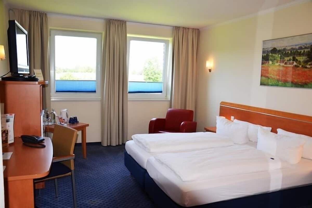 Habitación de hotel con cama, escritorio con silla, televisor y un cuadro en la pared.