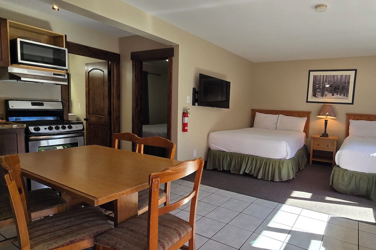 A hotel room with a kitchenette, two beds, a TV, and a window with curtains.