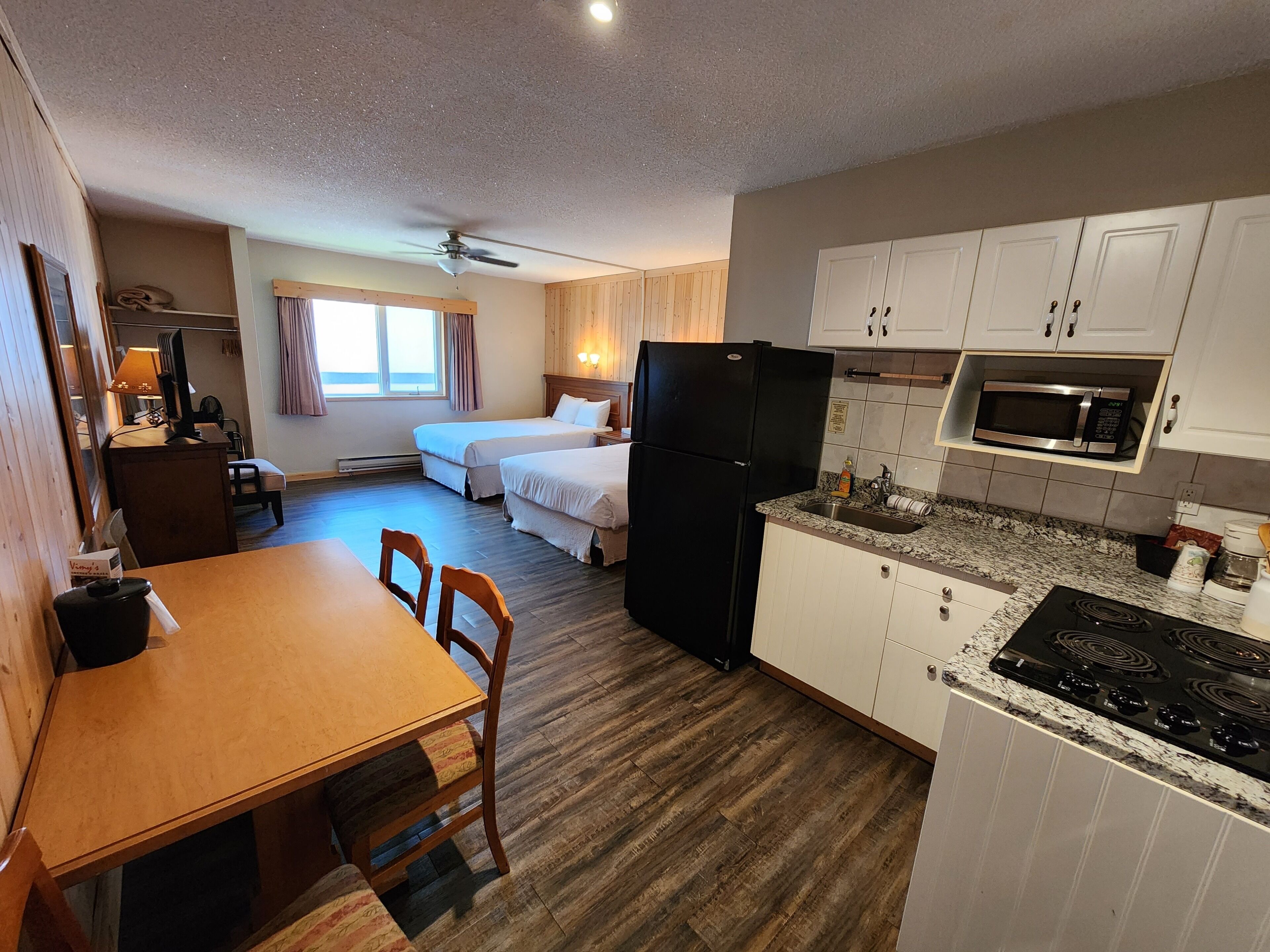 Habitación de hotel compacta con kitchenette, dos camas, zona de comedor y ventilador de techo.