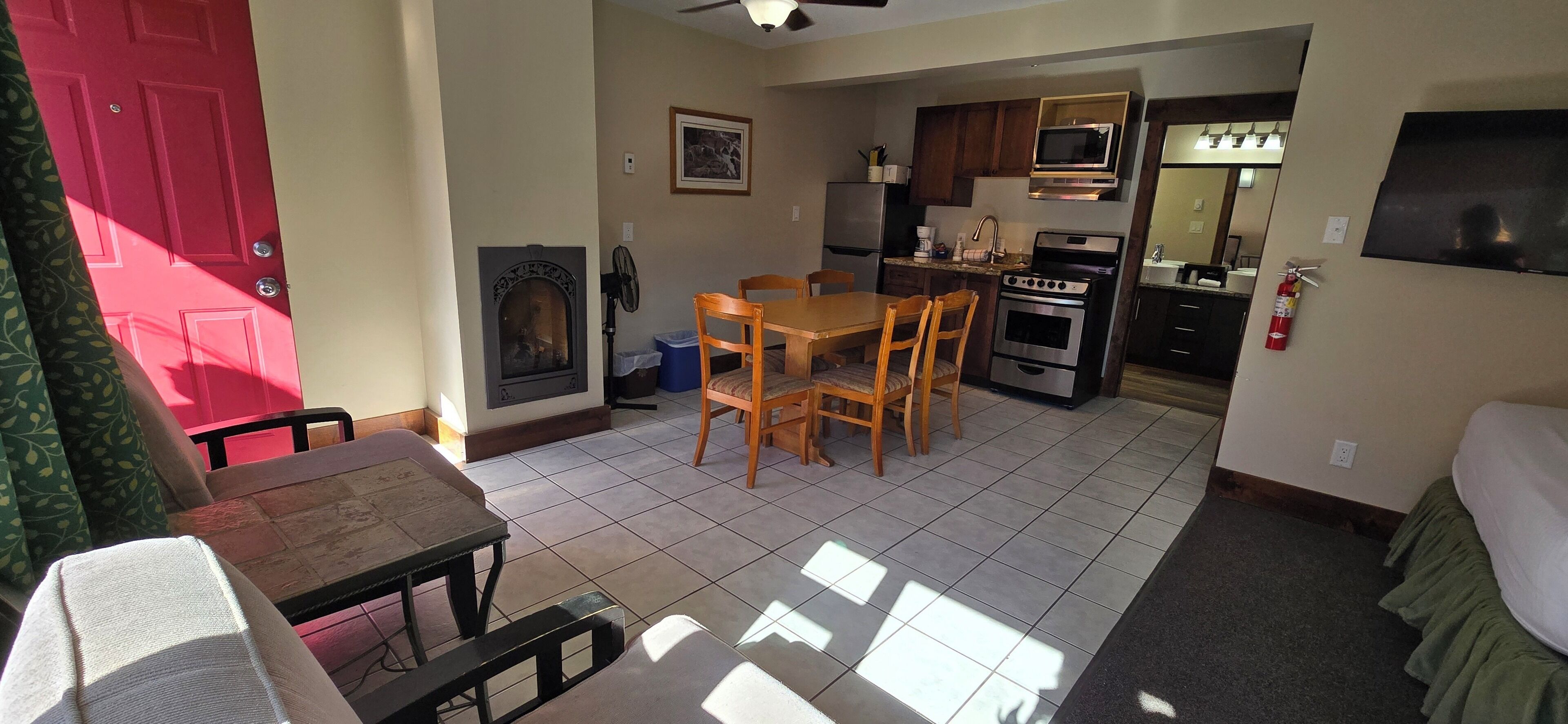 A compact kitchen with a microwave, oven, and refrigerator. There is a dining table with chairs and a fireplace.