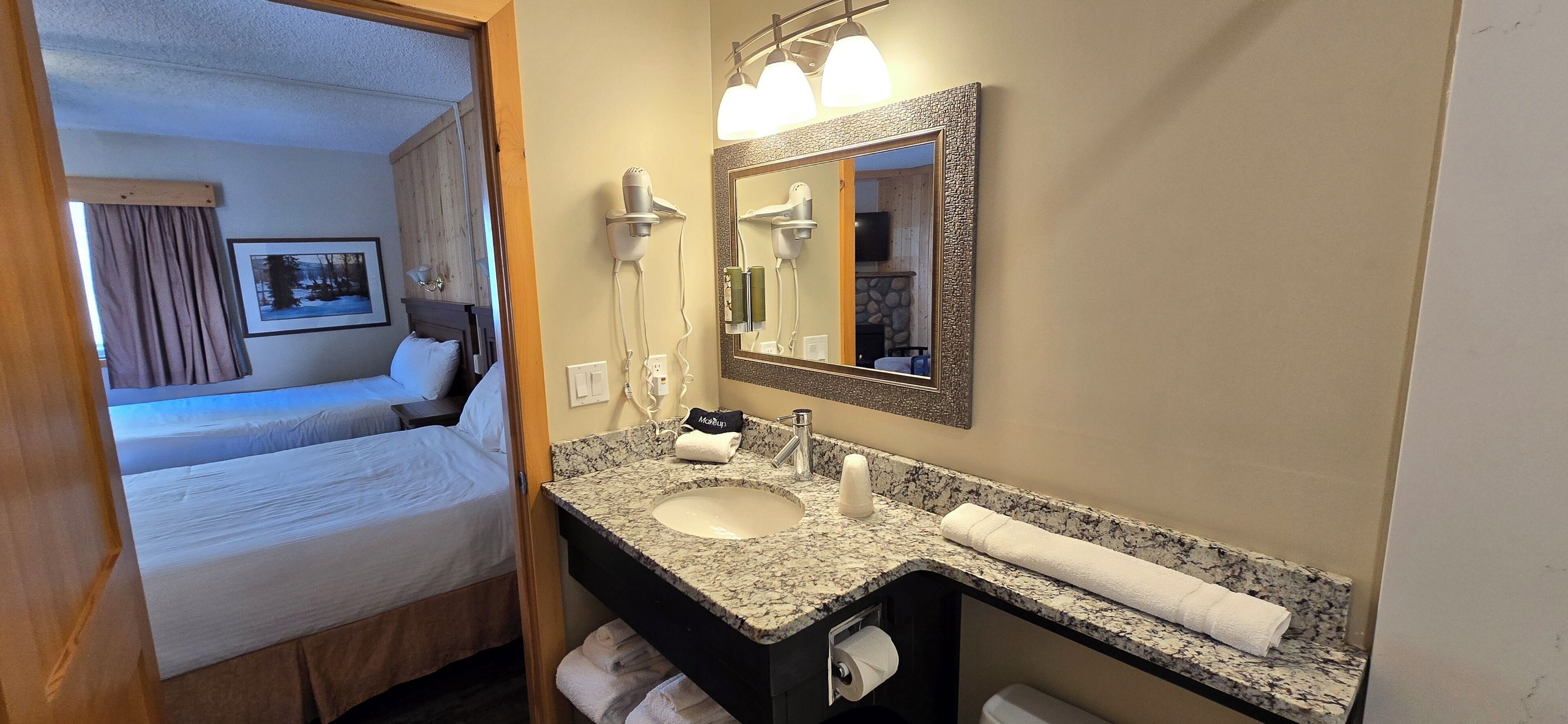 Una habitación de hotel con una cama, un baño con lavamanos, un espejo y un perchero para toallas.