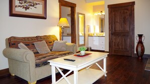 A living room with a sofa, a coffee table, a lamp, a mirror, and a door. - Aspen Village Inn (Waterton Park)