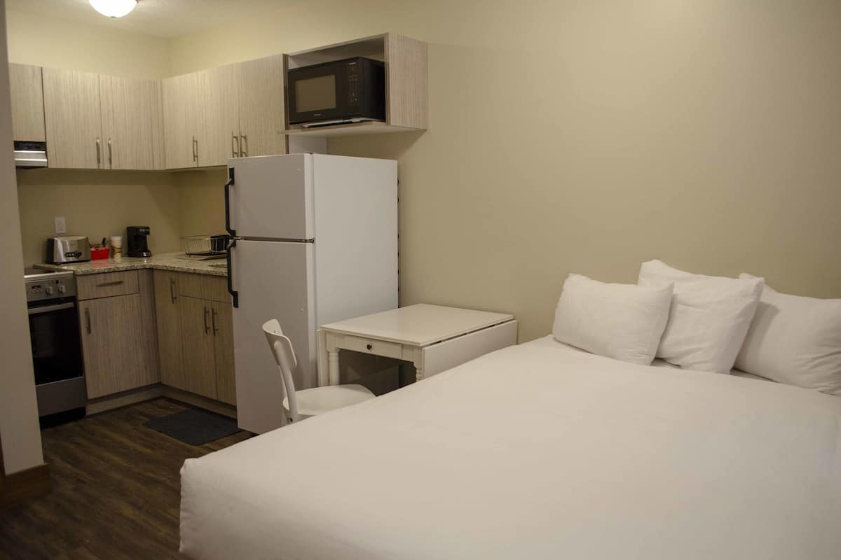 A compact hotel room with a kitchenette, a bed, and a small table.