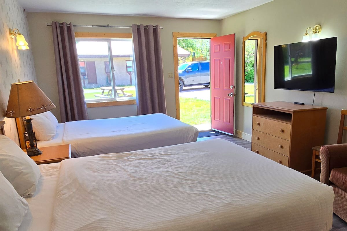 A hotel room with two beds, a TV, a dresser, a chair, and a window with curtains.