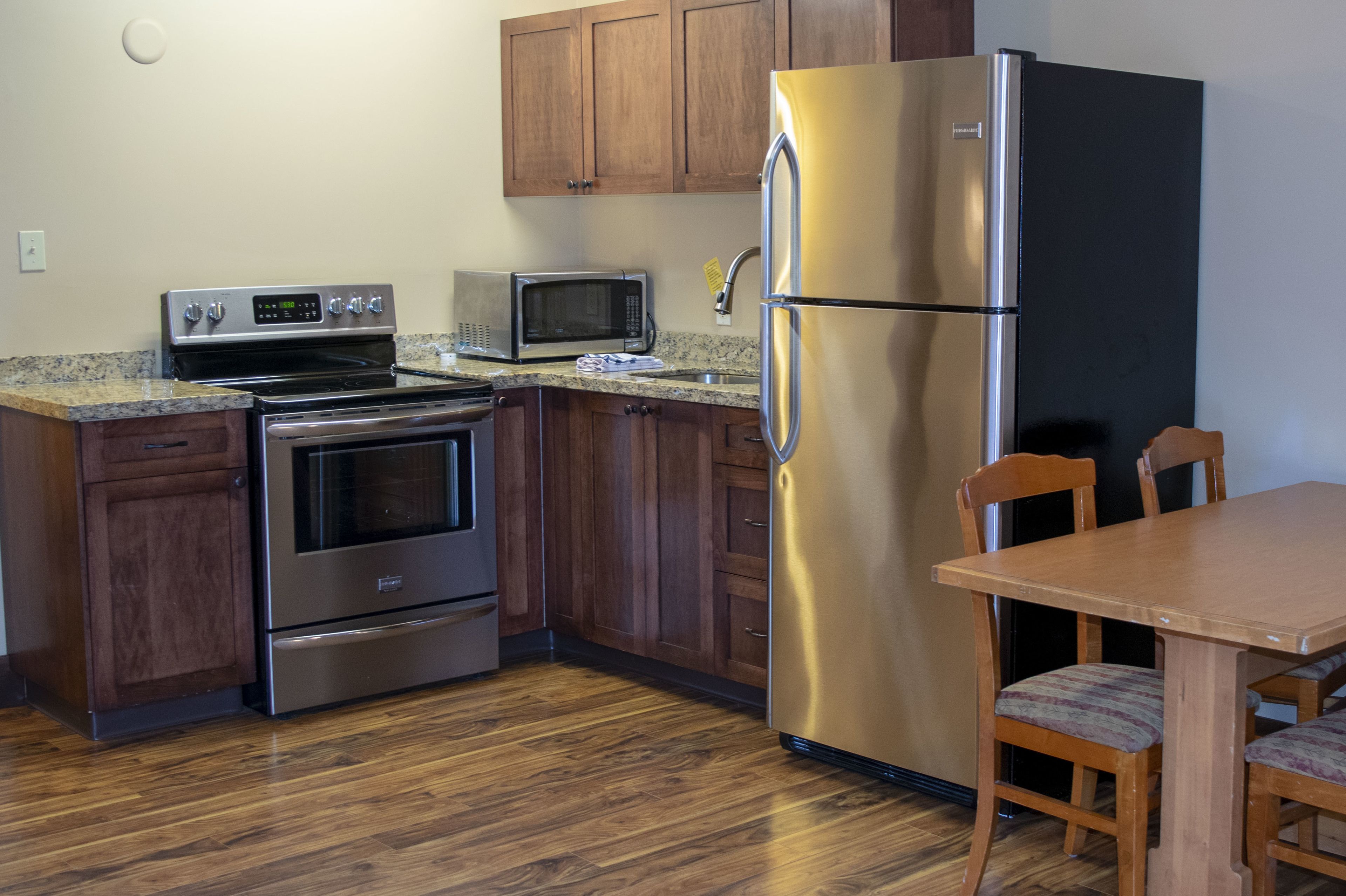 A kitchen with stainless steel appliances, wooden cabinets, and a dining table with chairs.