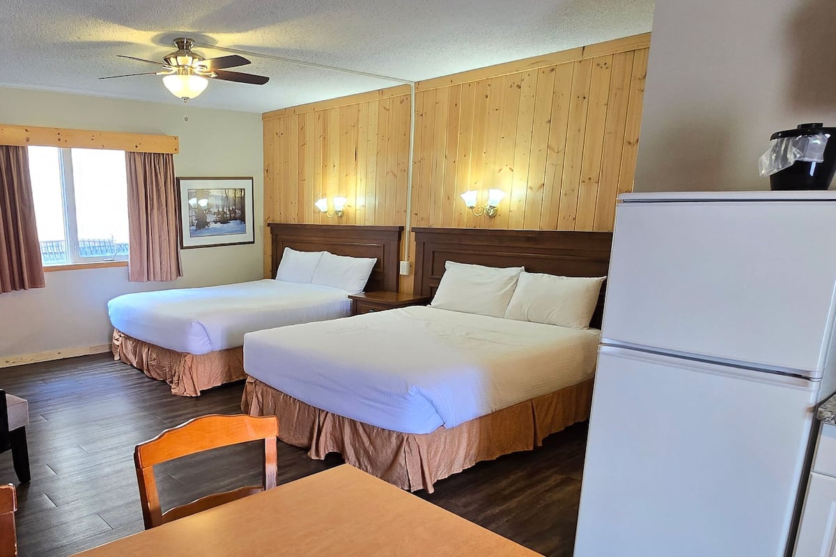 A room with two beds, a television, a stone fireplace, a ceiling fan, and a refrigerator.