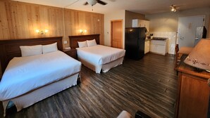 A hotel room with two beds, a ceiling fan, a refrigerator, a kitchenette, and wooden paneling on the walls. - Aspen Village Inn (Waterton Park)