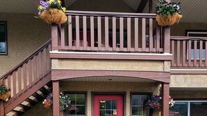 A two-story building with a red front door, stone foundation, and a balcony with hanging flower baskets. - Aspen Village Inn (Waterton Park)