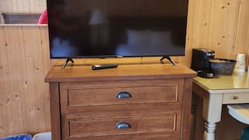 Een houten kast met een flatscreen televisie erop, een plafondventilator erboven en een klein tafeltje met een koffiezetapparaat en een kom.