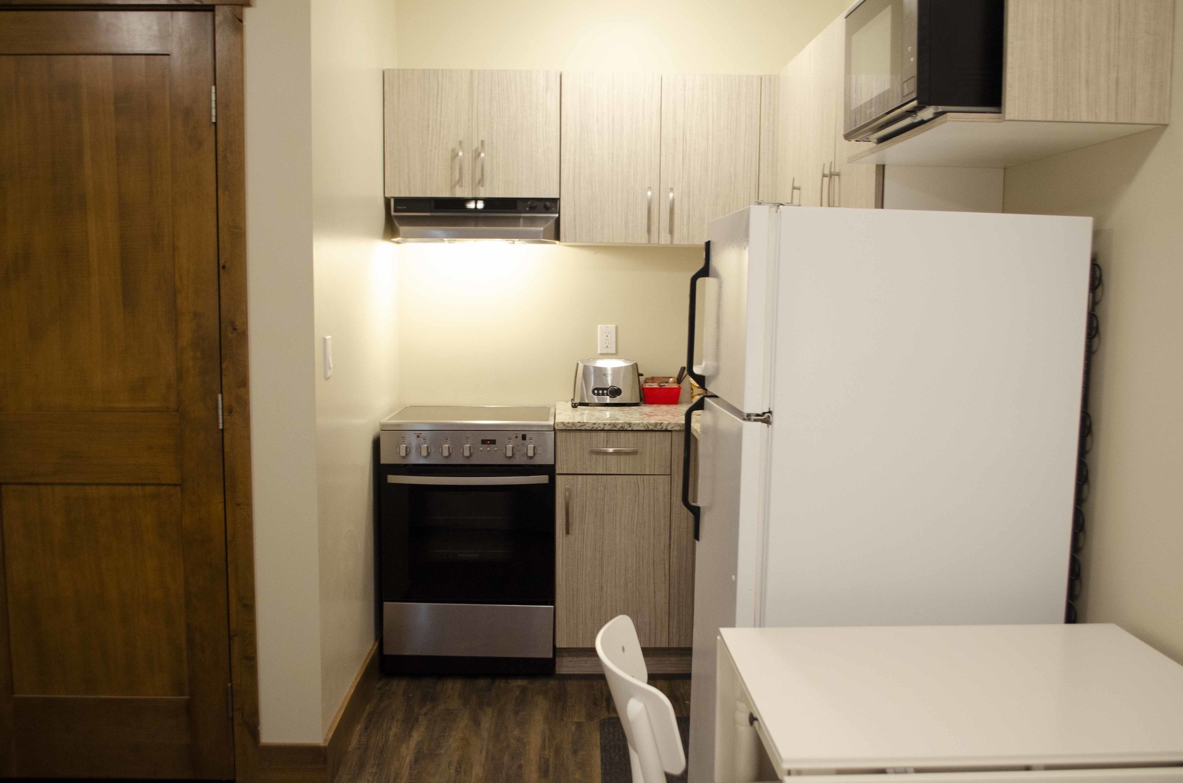 A compact kitchen with a refrigerator, oven, microwave, and a coffee maker on the countertop.