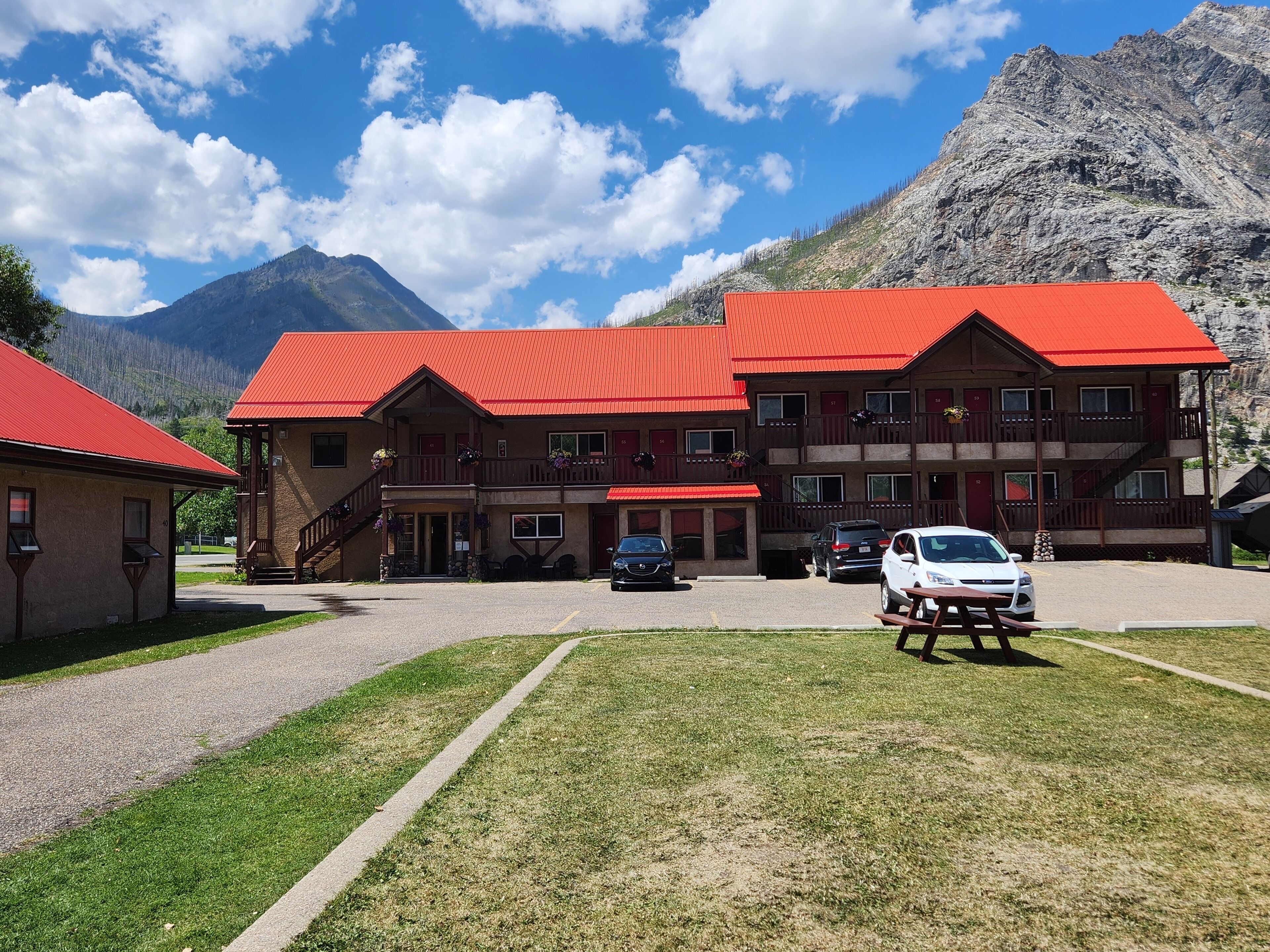 A multi-story building with a red roof, a covered parking area, and a picnic table in the foreground.