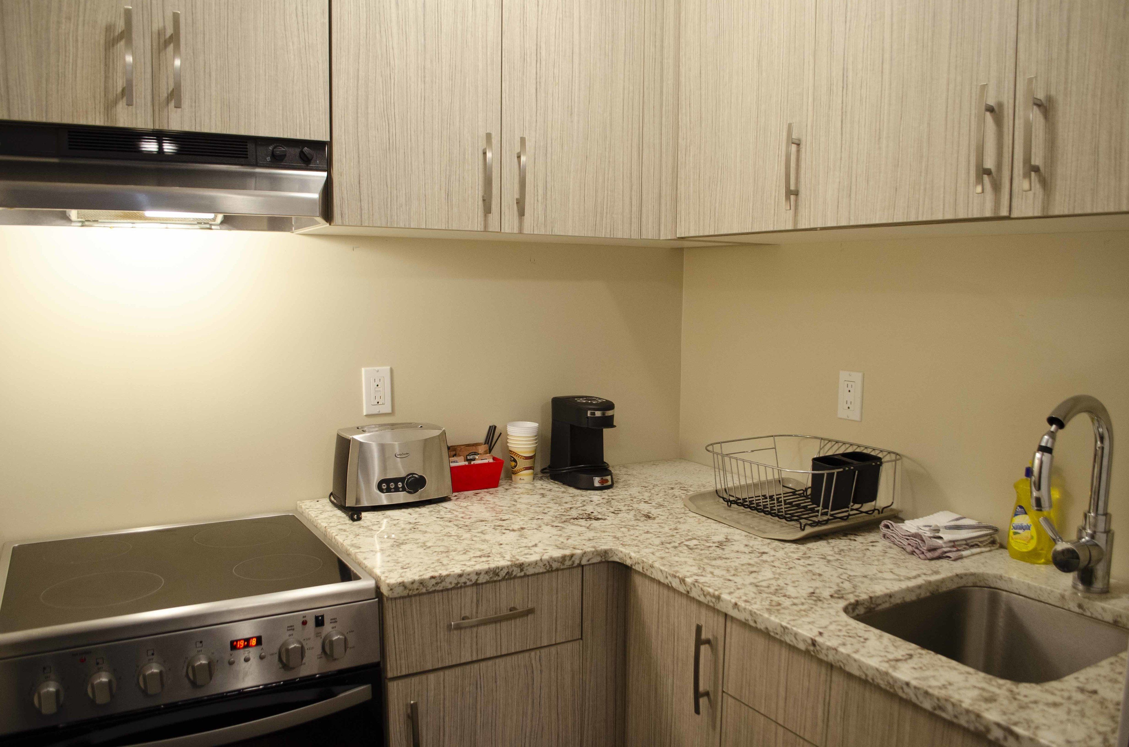 A kitchen with a stove, toaster, coffee maker, sink, and cabinets.