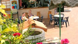 An outdoor seating area with tables and chairs, a thatched roof, and a bar in the background. - Alondras Park Apartamentos (Arona)