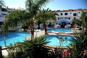 A swimming pool surrounded by palm trees and lounge chairs, with a building in the background. - Alondras Park Apartamentos (Arona)