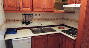 A kitchen with wooden cabinets, a stainless steel sink, a stove, and a dish rack.