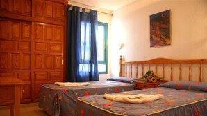 A room with two beds, a wooden wardrobe, a window with curtains, and a painting on the wall. - Alondras Park Apartamentos (Arona)
