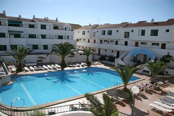 A swimming pool with lounge chairs and palm trees, surrounded by multi-story buildings.
