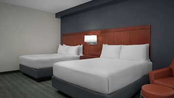 Ein Hotelzimmer mit zwei Betten, einem Nachttisch, einer Lampe und einem Sessel.