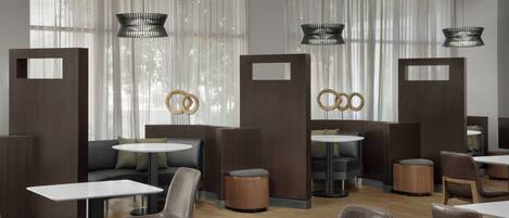 Un moderno vestíbulo de hotel con mesas redondas, asientos cómodos e iluminación decorativa.