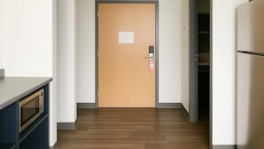 Un pasillo con puerta de madera, microondas y refrigerador.