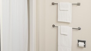 Un baño con una bañera, dos barras para toallas con toallas blancas, un inodoro y una cortina de ducha.