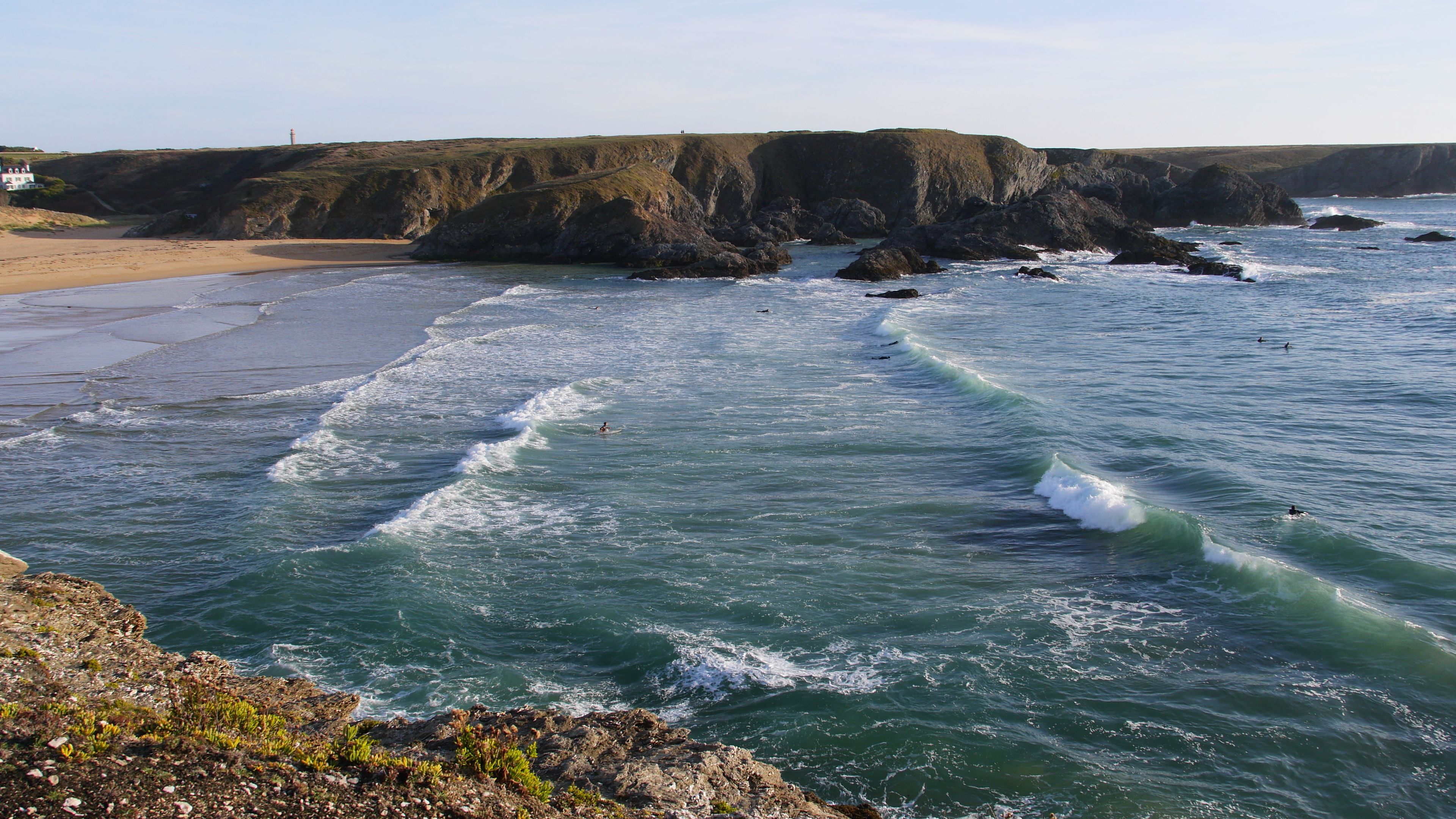 A coastal landscape with a beach, rocky cliffs, and waves crashing onto the shore.
