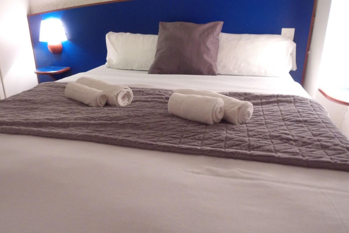 A neatly made bed with a quilted blanket, two rolled towels, and a pillow.