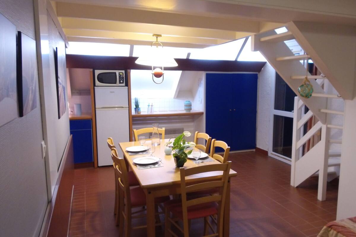 A compact kitchen with a microwave, a dining table set for four, and a staircase leading to an upper level.