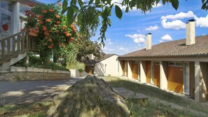 A residential building with a stone wall, a large rock in the foreground, and a tree with red flowers. - VVF Lac d'Eguzon, Eguzon Chantôme (Eguzon-Chantome)
