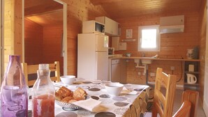 Puinen mökki, jossa on ruokapöytä kahdelle, jääkaappi, mikroaaltouuni ja pesuallas keittiöalueella.