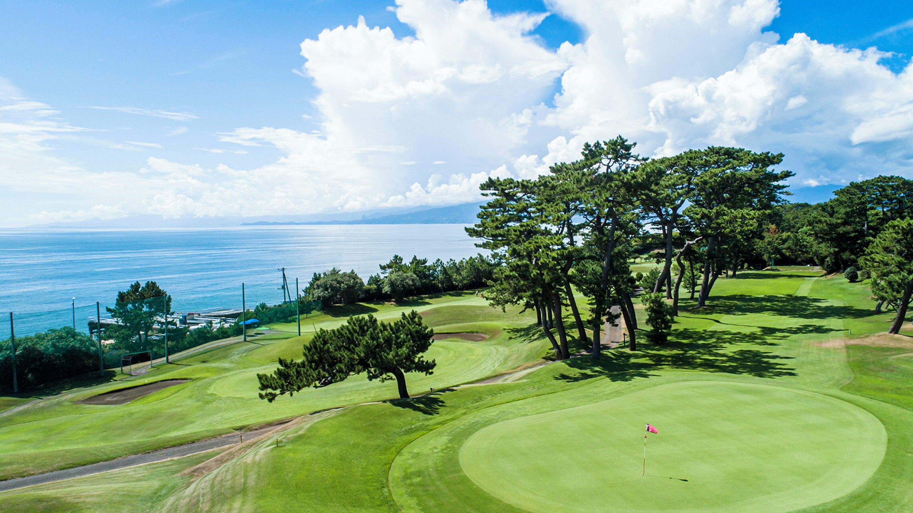 Un campo de golf con vista al océano, rodeado de árboles y un cielo despejado.