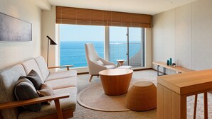 A modern living room with a sofa, armchair, coffee table, and a view of the ocean through large windows. - Oiso Prince Hotel (Oiso)