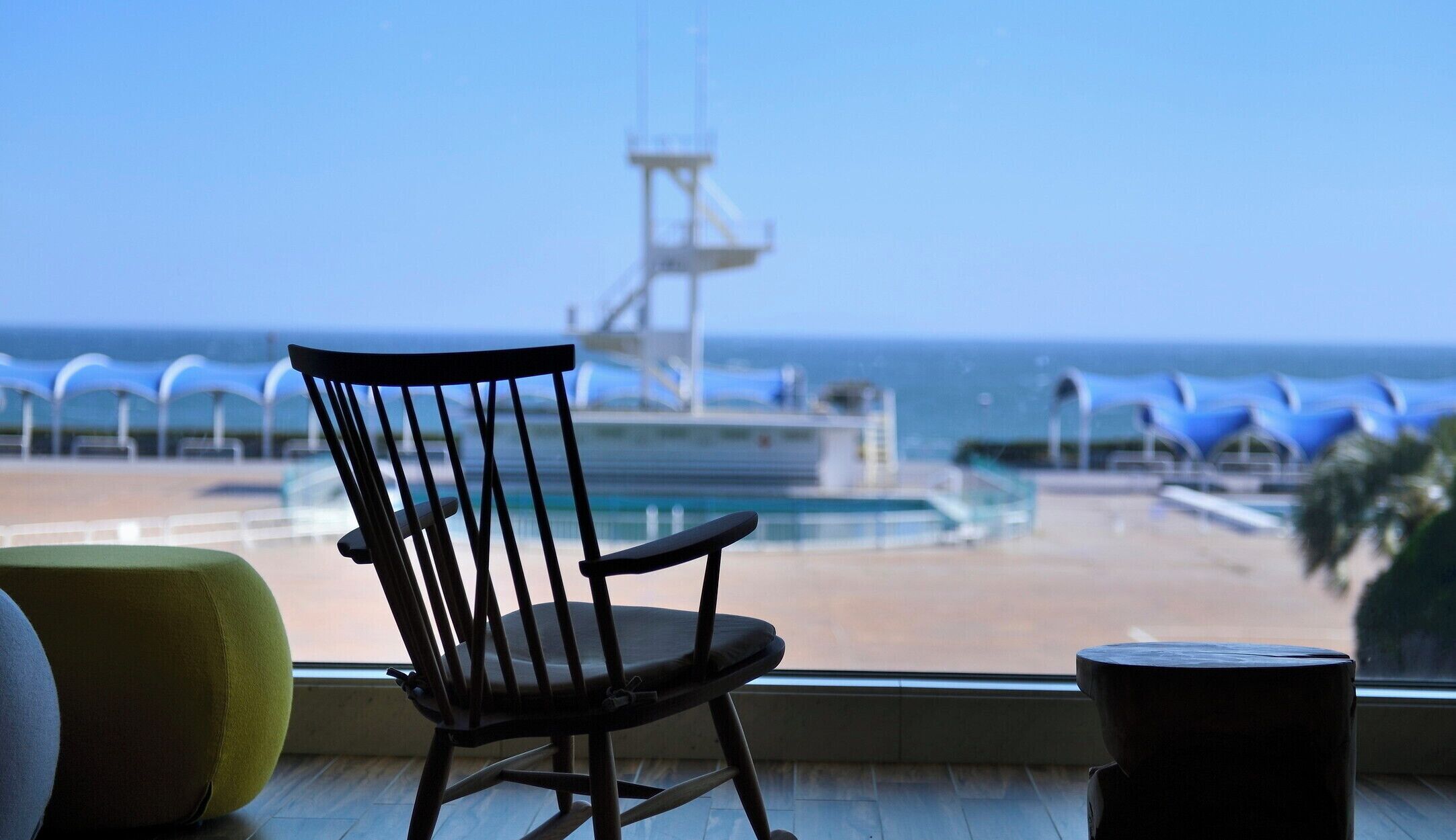A chair by a window overlooking a beach with umbrellas and a lifeguard tower.