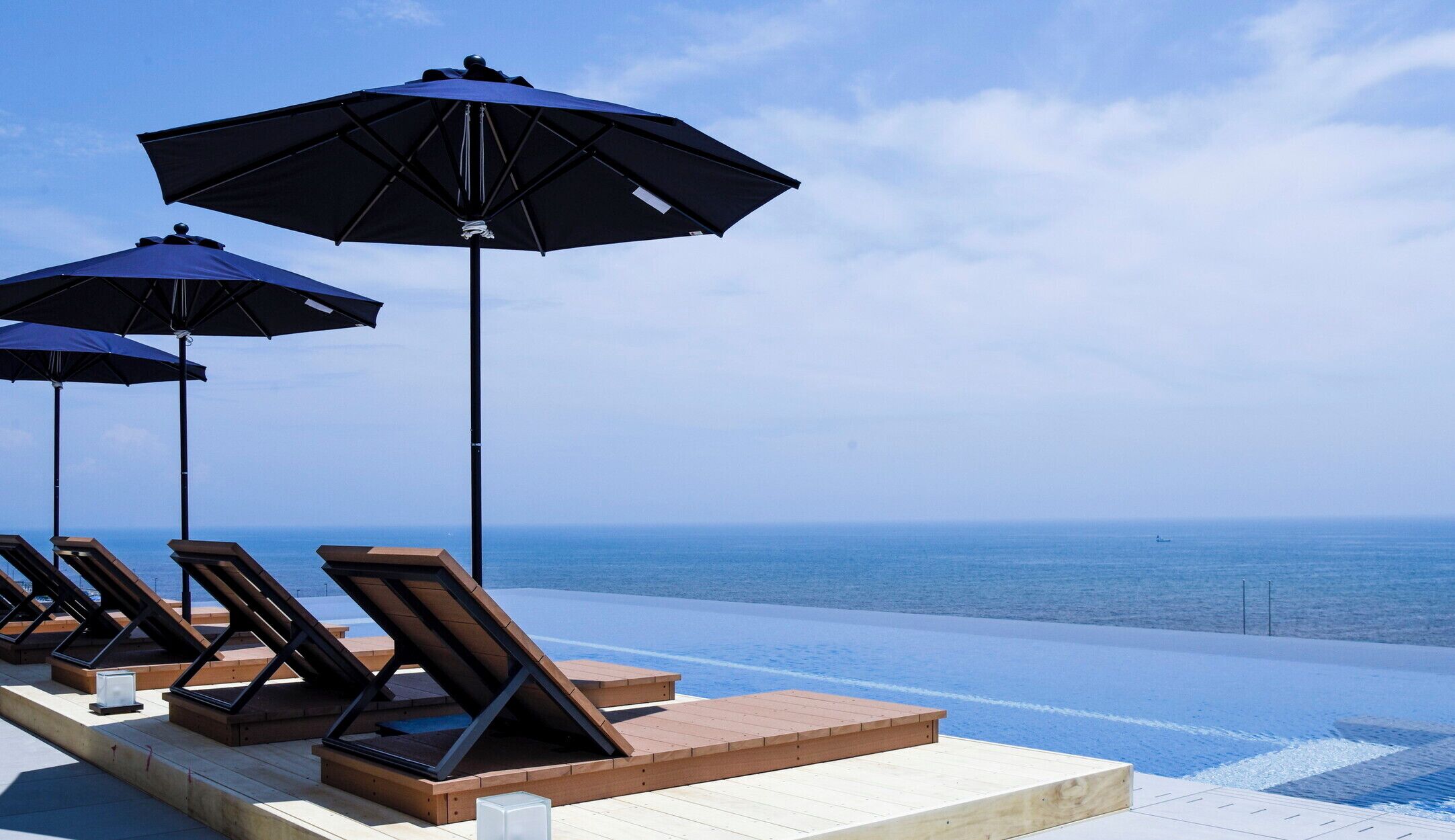 An infinity pool with lounge chairs and umbrellas, overlooking the sea.