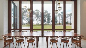 A dining area with a large table and chairs, large windows with a view of a grassy area and trees. - Oiso Prince Hotel (Oiso)