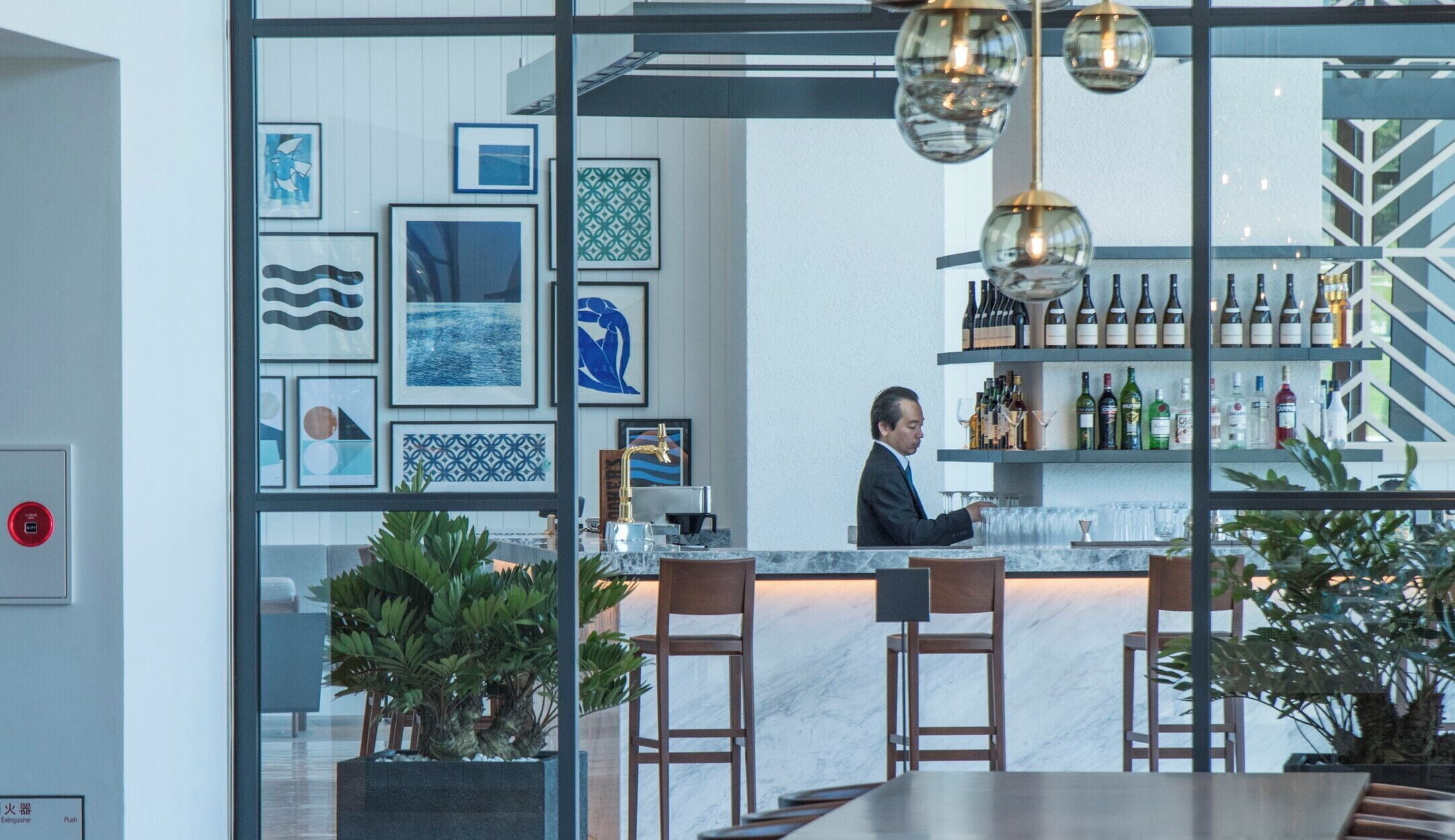 A modern bar area with a bartender, marble countertops, and a variety of bottles and glasses.