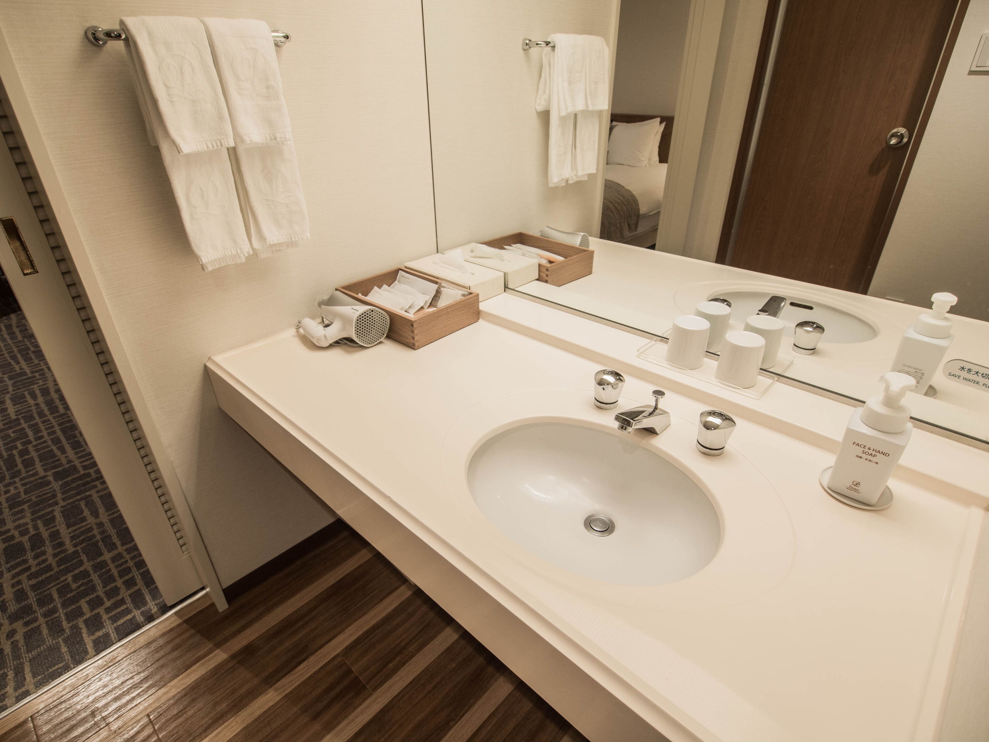 A modern bathroom with a large mirror, two sinks, and a wooden box with toiletries.