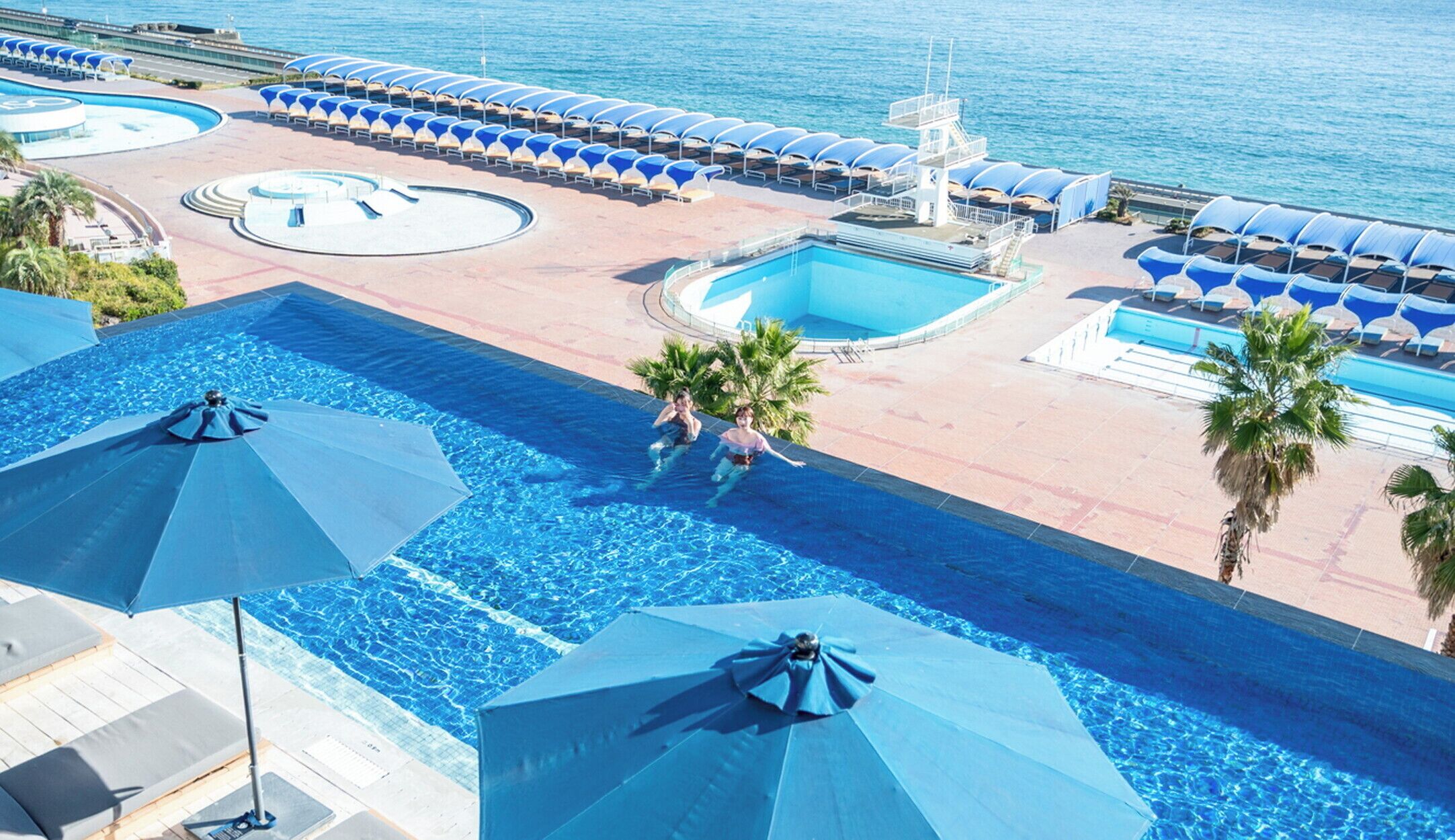 Ein Poolbereich mit mehreren Schwimmbecken, Liegestühlen und Sonnenschirmen.