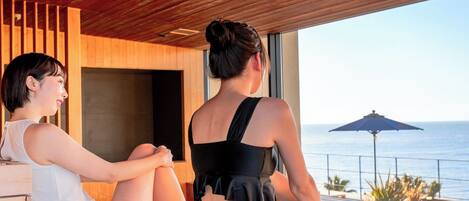 Two people sitting by a window overlooking the ocean, with a wooden ceiling and a view of the sea.